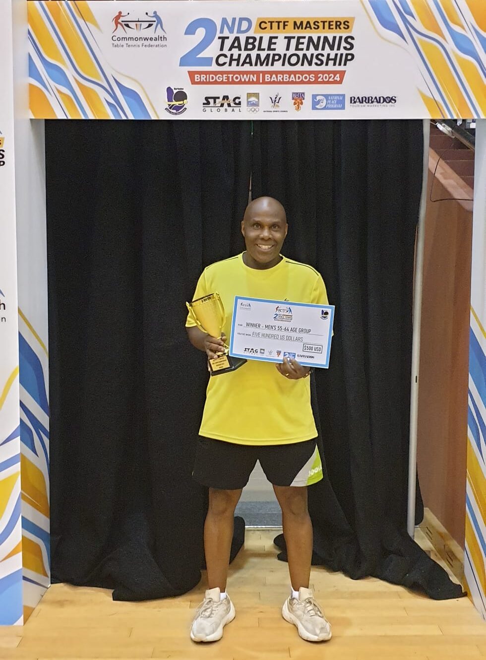 Dave holding a gold cup and certificate winning the Commonwealth Masters table tennis 55-64 age category.